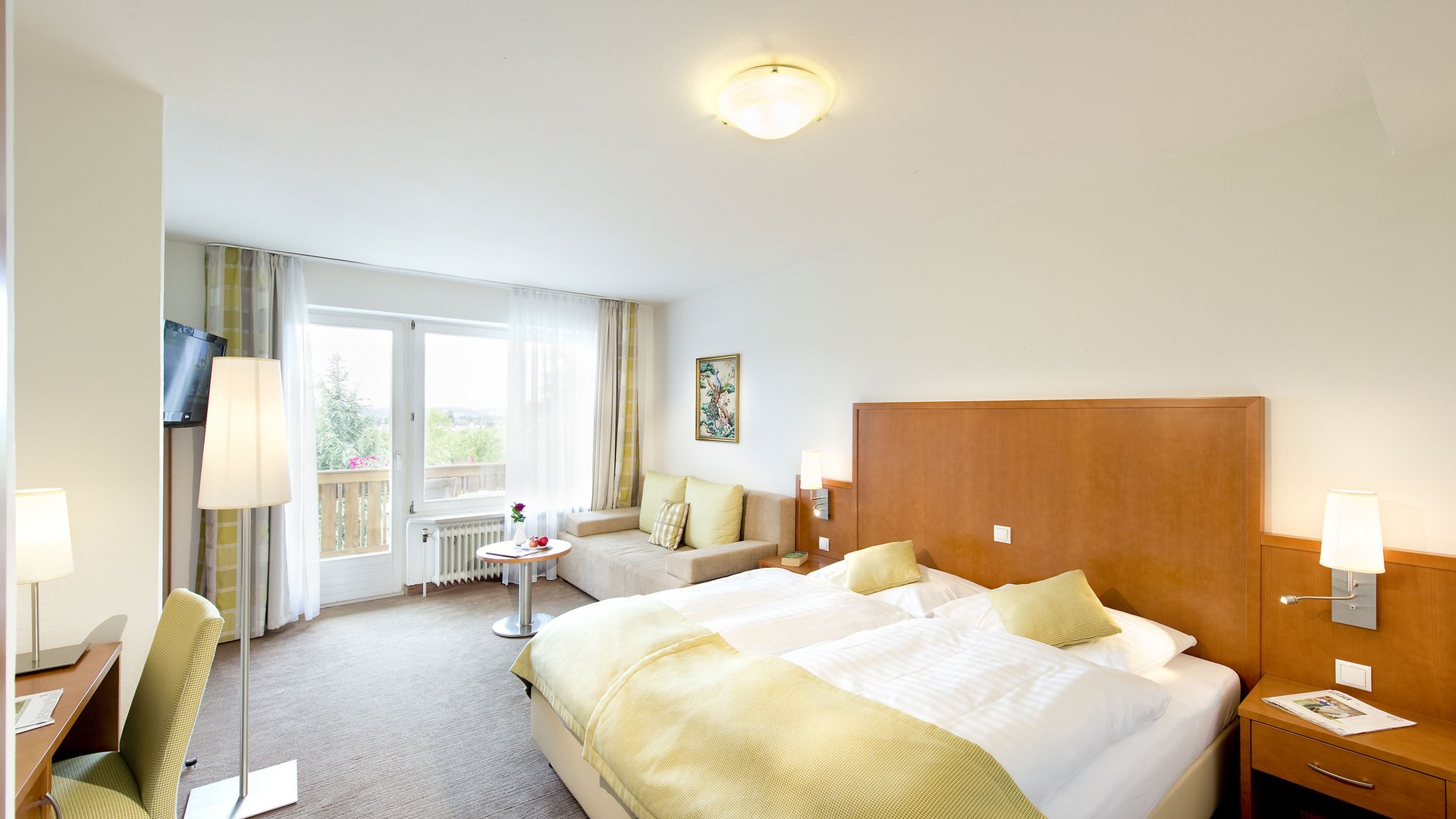 Bright hotel room with double bed, sofa, and balcony