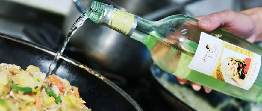 Flüssigkeit wird aus einer grünen Flasche in eine Pfanne mit Gemüse gegossen
