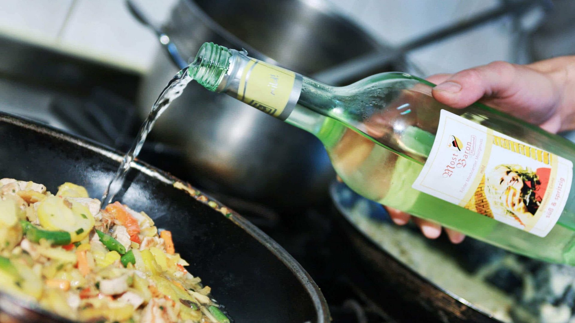Liquid poured from a green bottle into a pan with vegetables