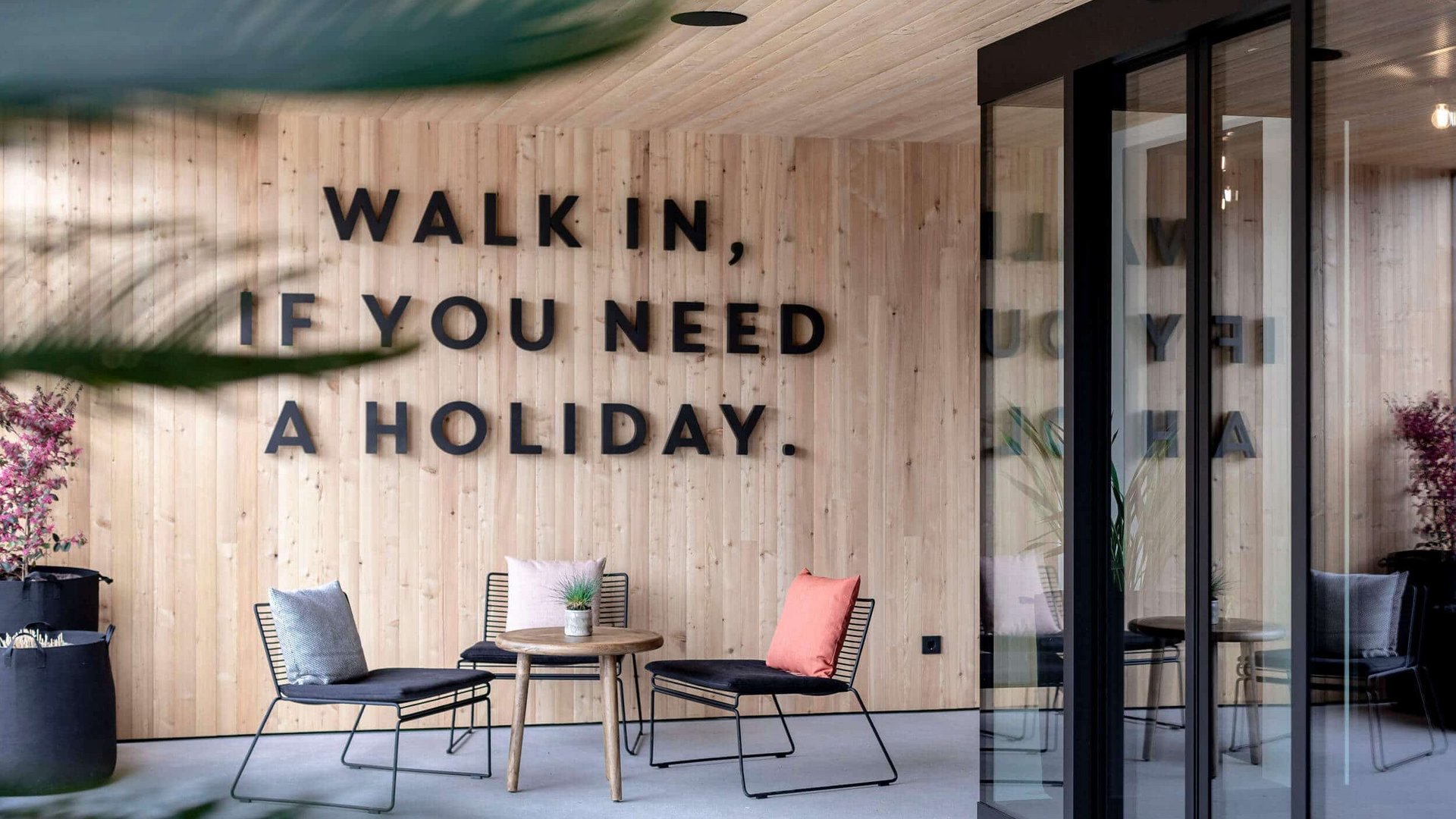 Seating area with chairs and wooden wall displaying "Walk in, if you need a holiday"