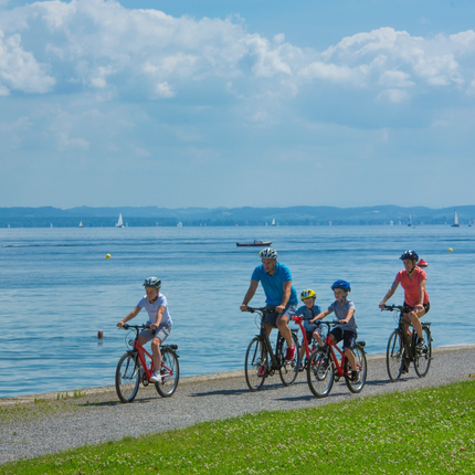 Family cycling on a path beside a lake on a sunny day
