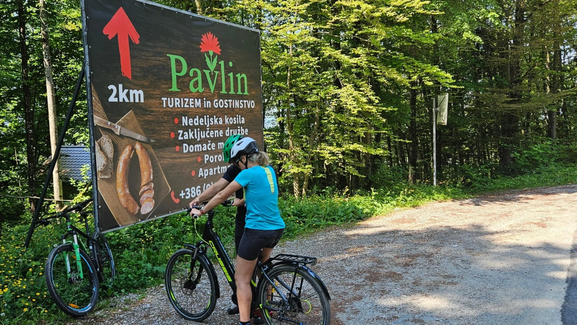 Fietsers bij een Pavlin bord 2 km verderop in een bosrijke omgeving
