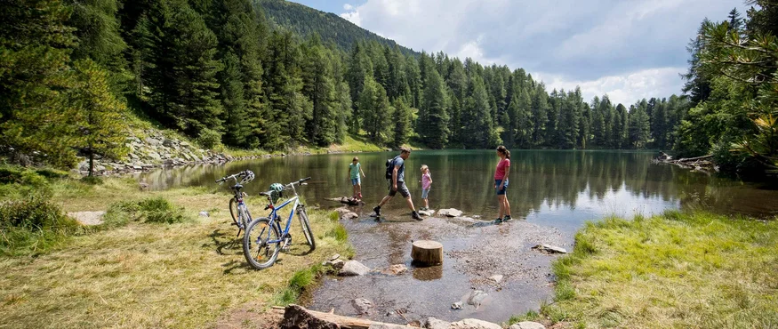 Familie am Seeufer mit Fahrrädern umgeben von Bergen und Wald