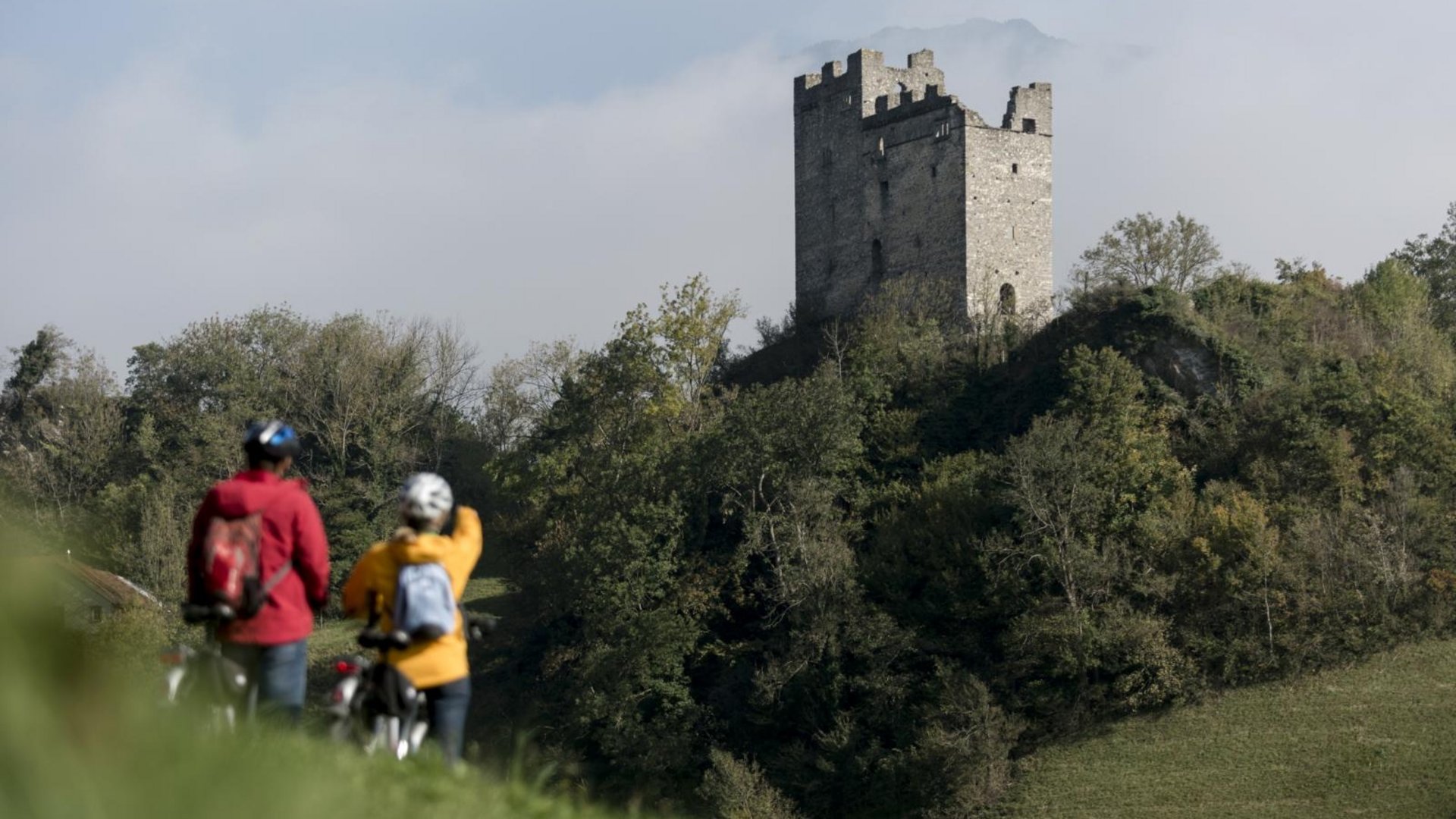 Two cyclists near an old castle ruin on a wooded hill