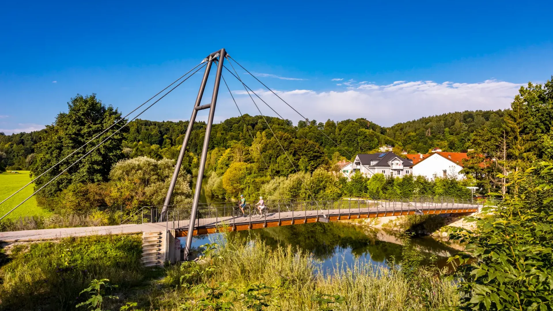 Fahrradfahrer auf einer Hängebrücke über einem Fluss in einer grünen Landschaft
