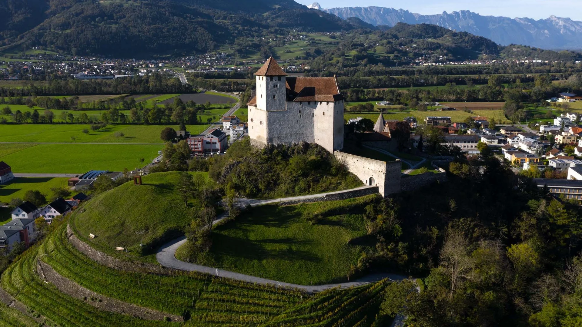 Kasteel op heuvel met groene velden en bergen op de achtergrond