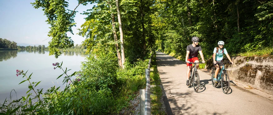 Zwei Radfahrer auf einem Weg neben einem Fluss im Wald