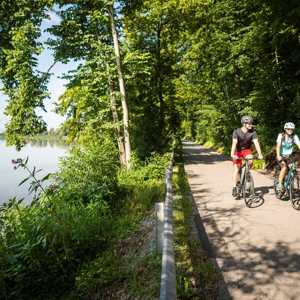 Immer am Wasser entlang im Chiemsee-Alpenland © Velontour Zwei Radfahrer auf einem Weg neben einem Fluss im Wald