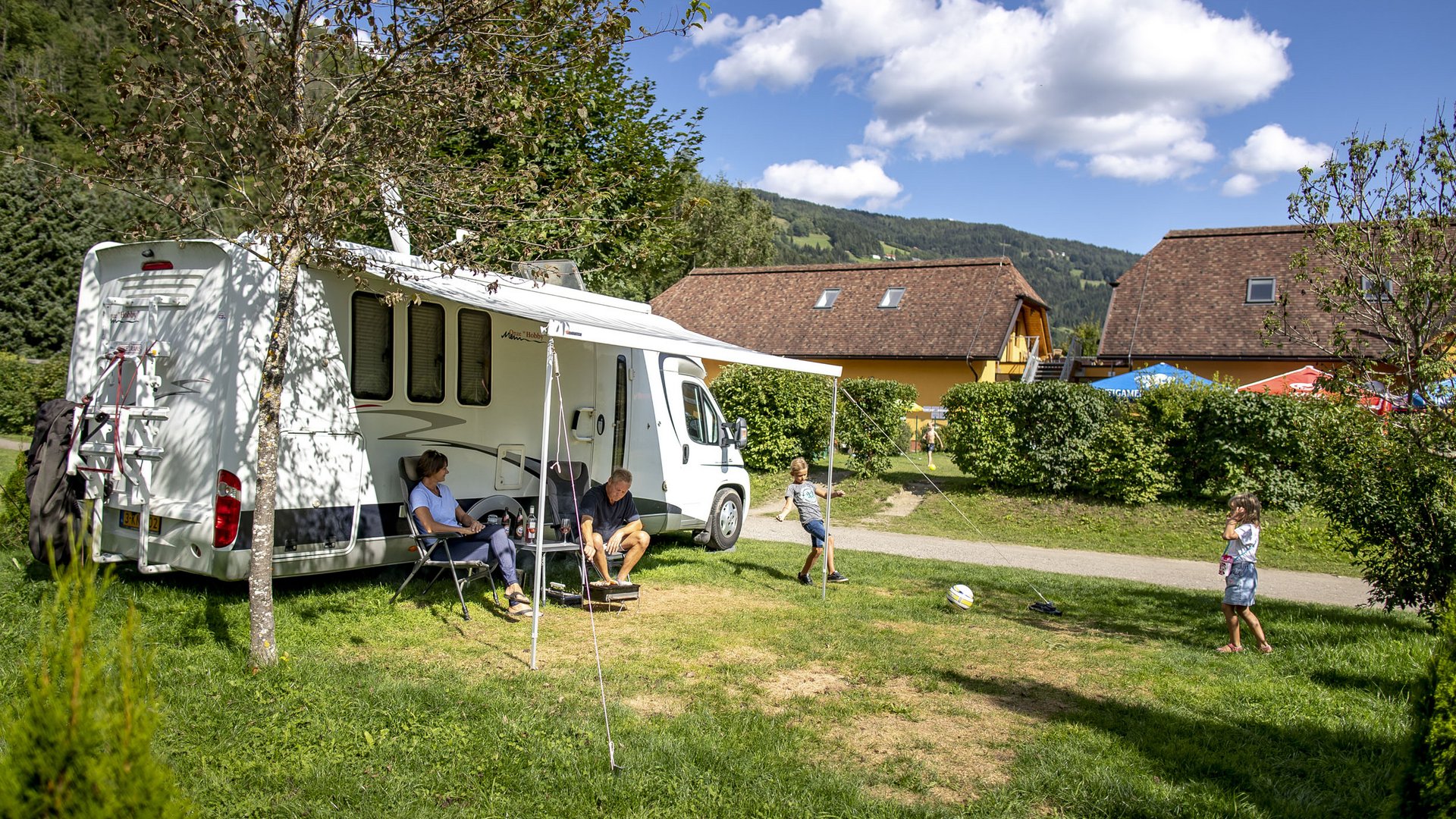 Family with children playing beside a camper at a campsite