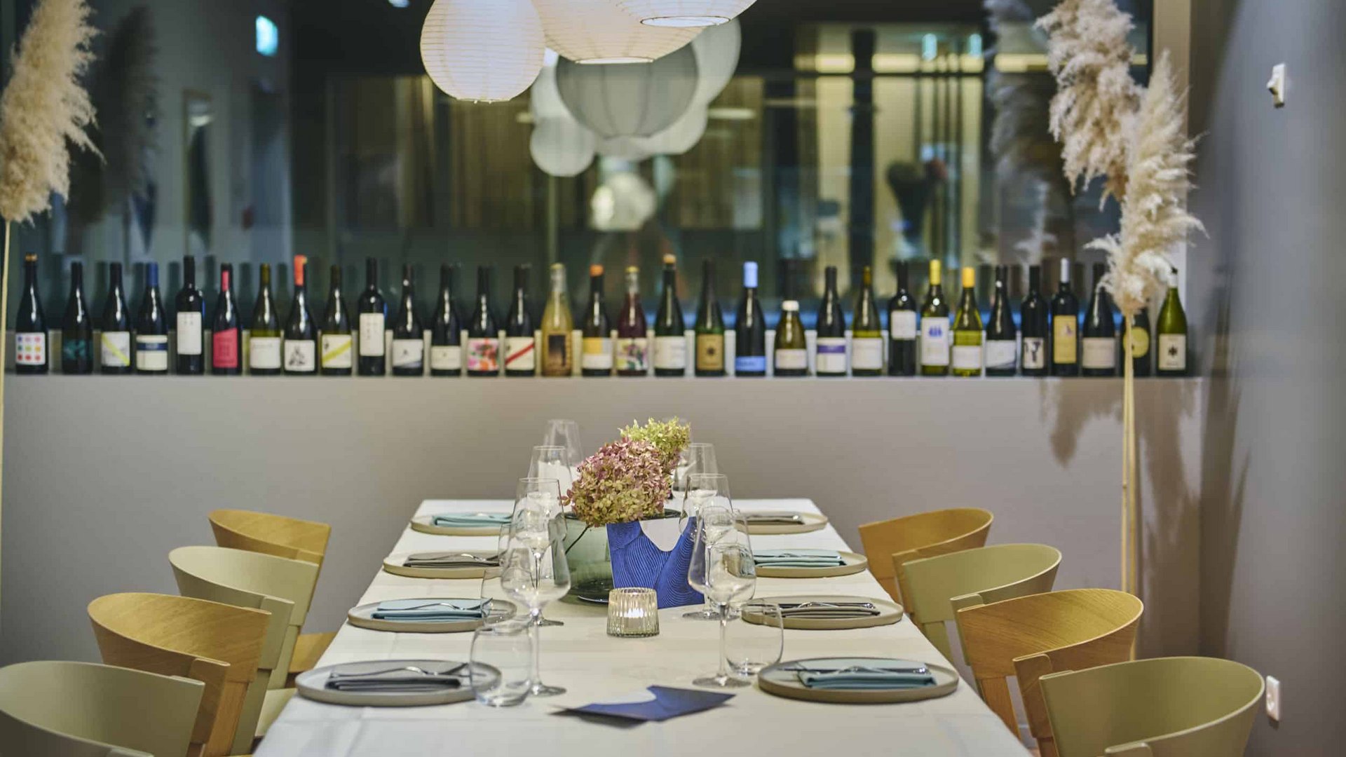 Elegant set dining table with wine bottles shelf and pendant lights in the background