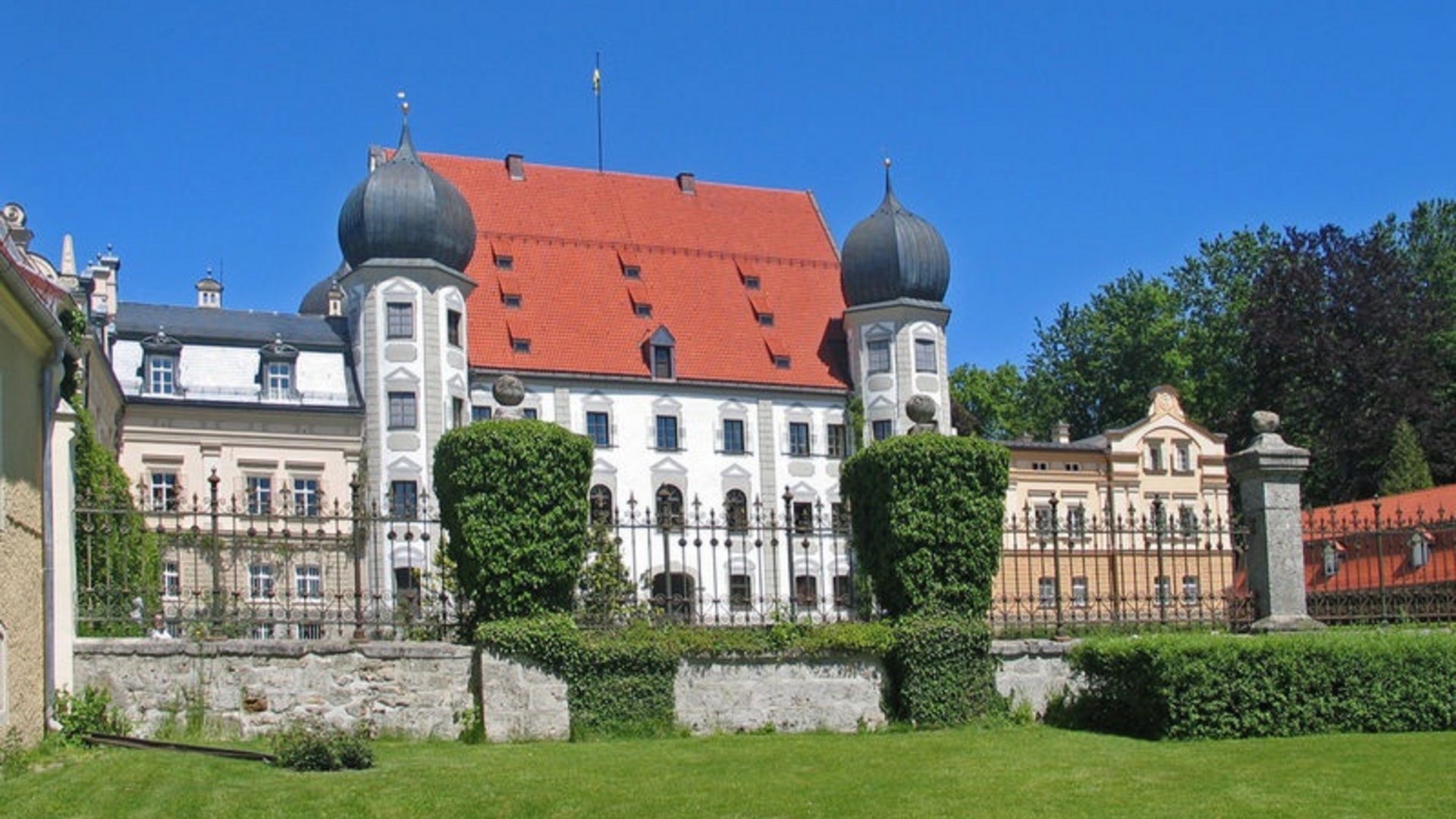 Baroque castle with red roofs and manicured garden under clear blue sky
