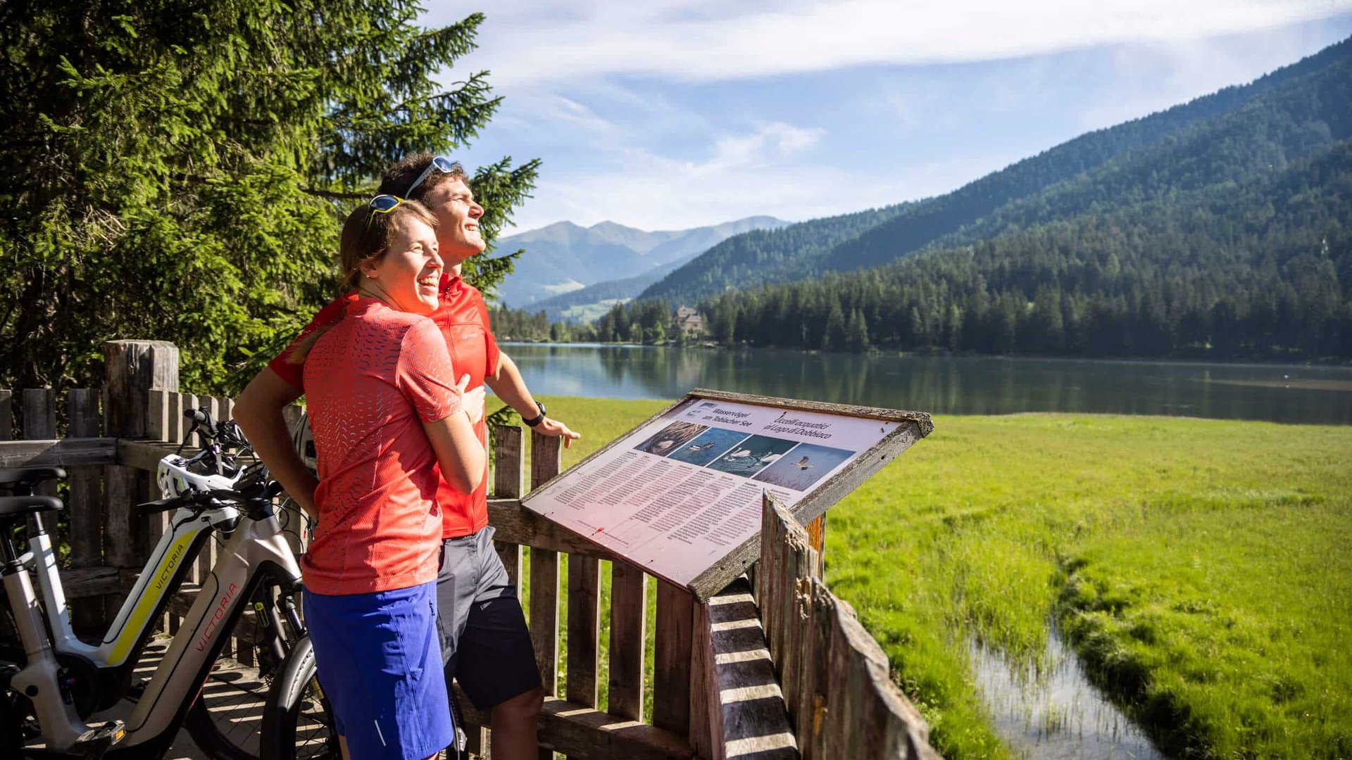 Couple with e-bikes enjoying view of lake and mountains on sunny day