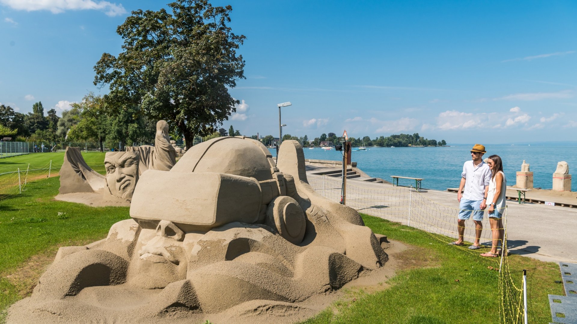 Sand art sculptures by the lakeside viewed by a couple on a sunny day