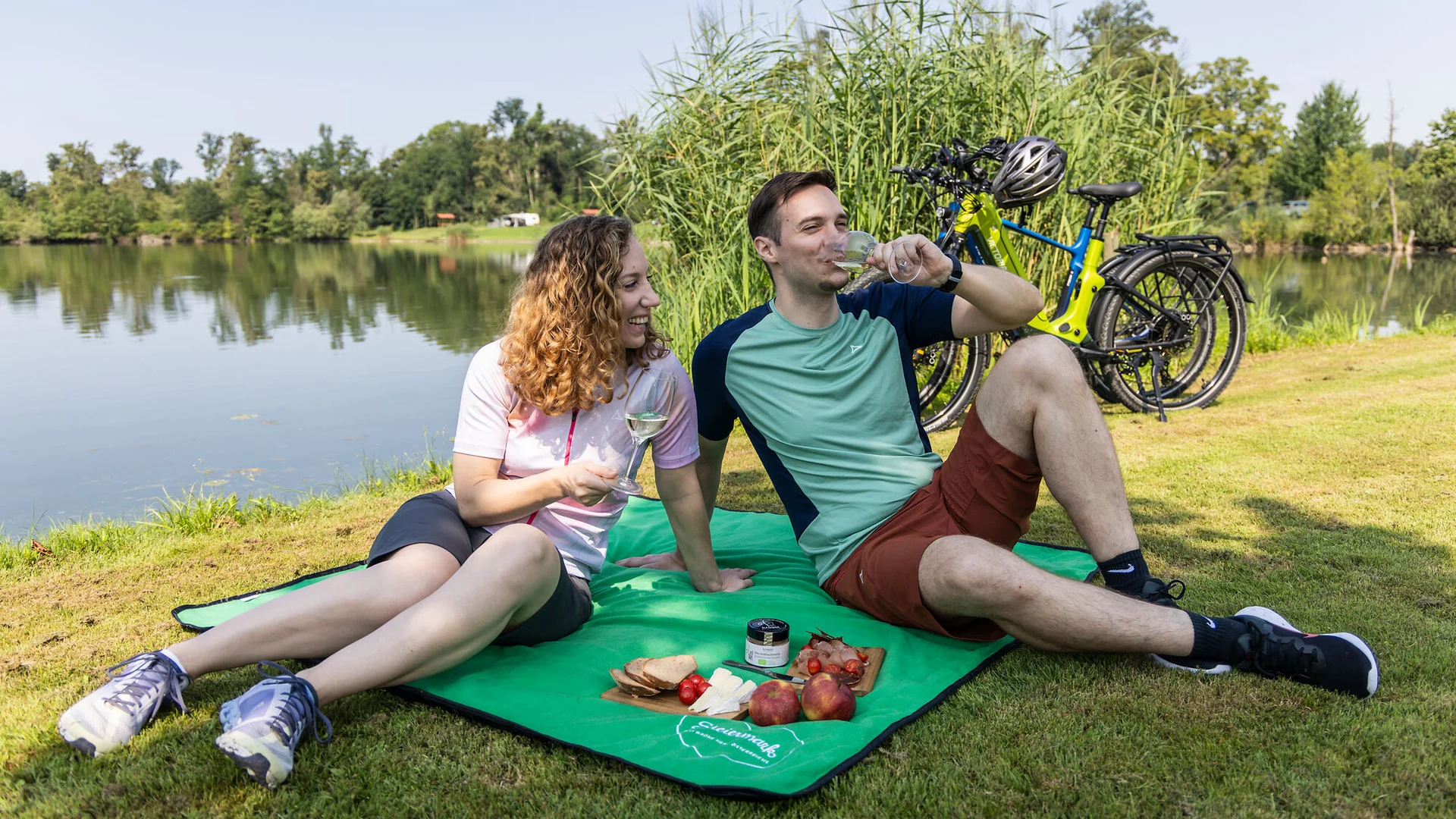 Genuss mit jedem Tritt im Thermen- & Vulkanland © Heiko Mandl Paar macht Picknick am See mit Fahrrädern im Hintergrund