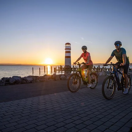 Twee fietsers fietsen langs het meer nabij een vuurtoren bij zonsondergang