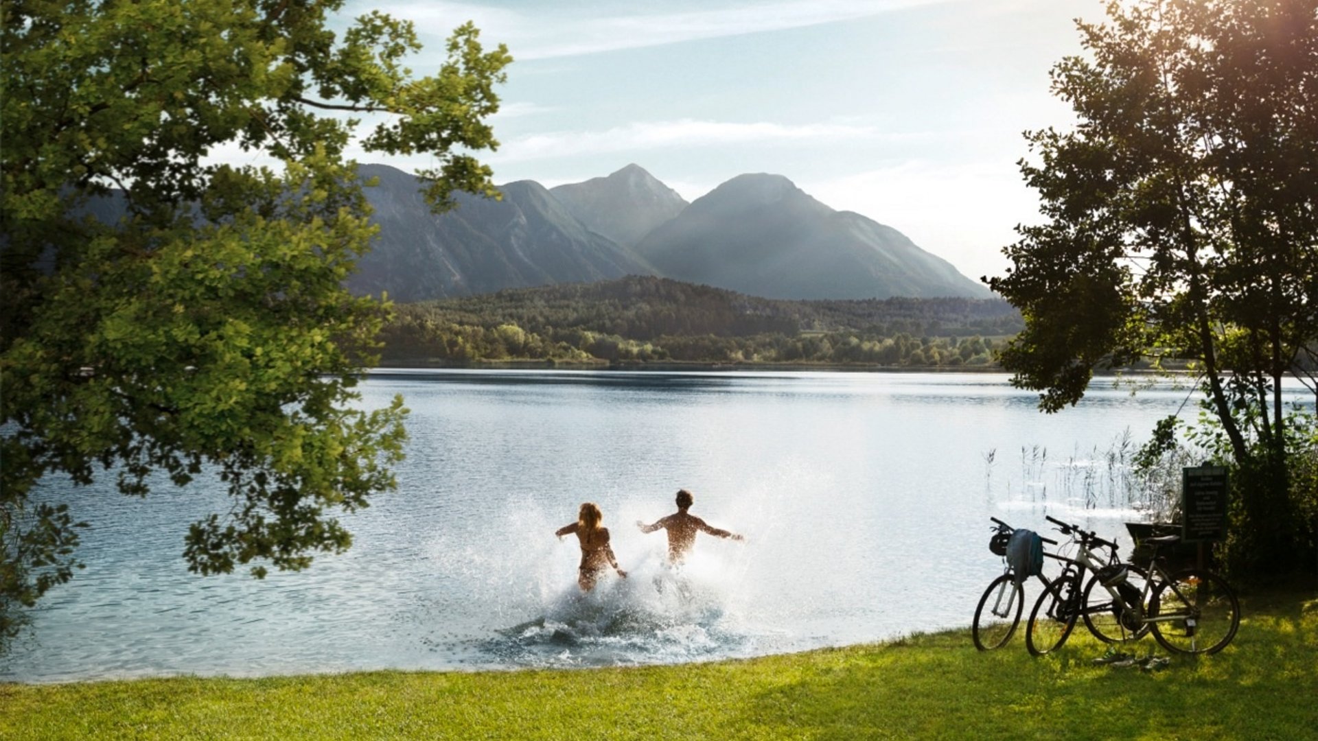 Two people jumping into a lake with mountains in the background