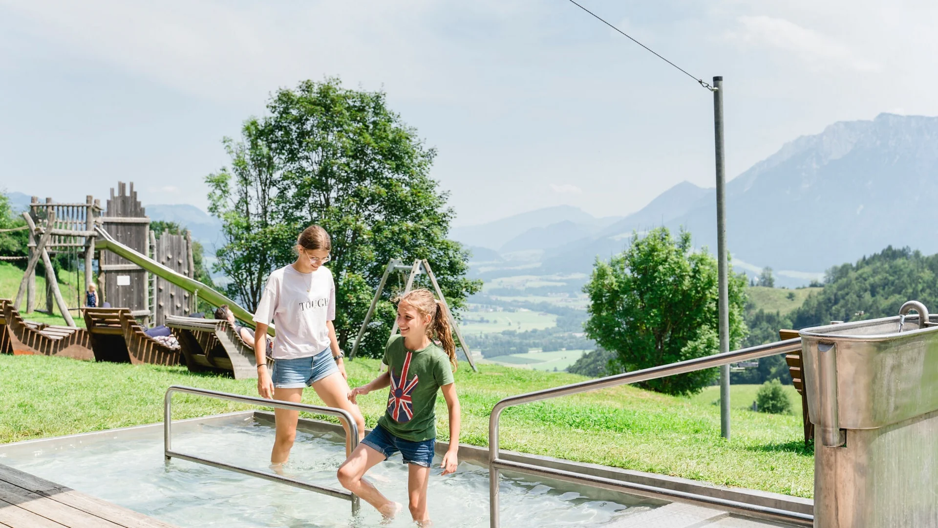 Zwei Mädchen bei einer Kneipp-Anlage mit Bergen im Hintergrund