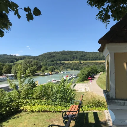 Blick auf Fluss mit Booten, Hügel und Bank unter Bäumen an Kapelle