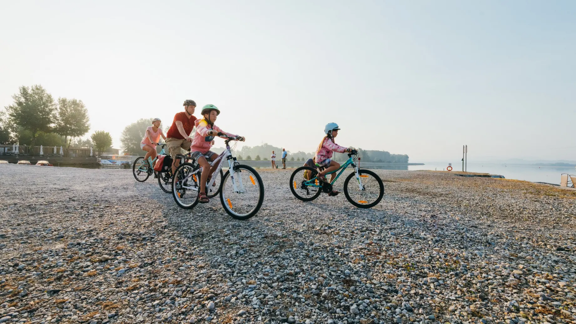 Family wearing helmets riding bikes on rocky shore by the lake