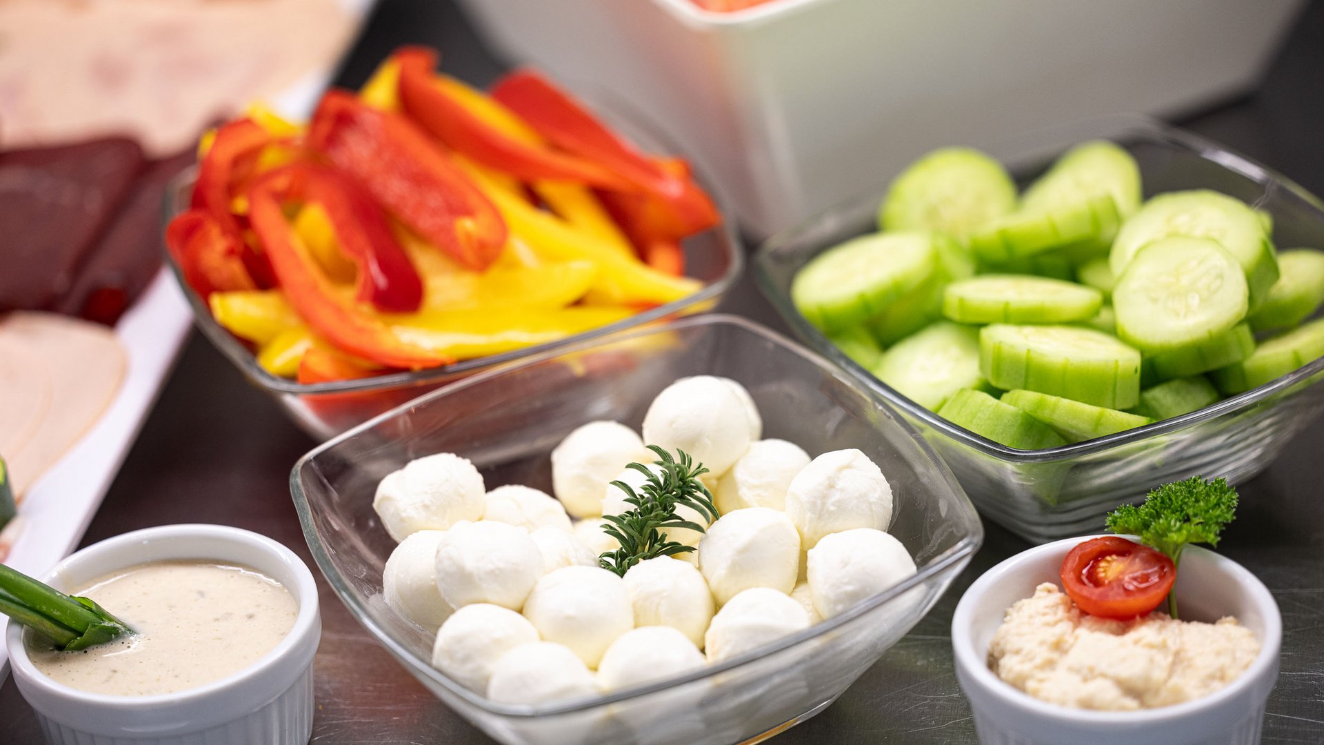 Bowls of bell peppers, cucumbers, mozzarella, and dips on a table