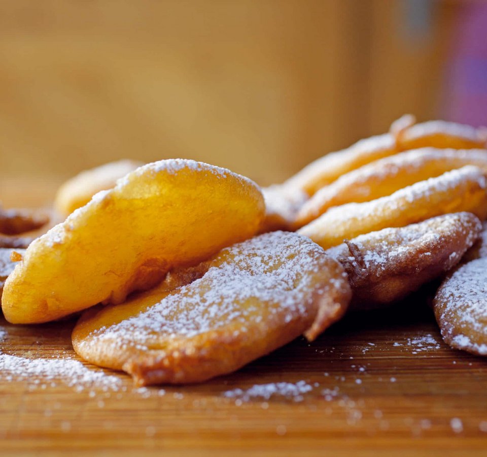 Fried sweet dough pieces dusted with powdered sugar on wooden board