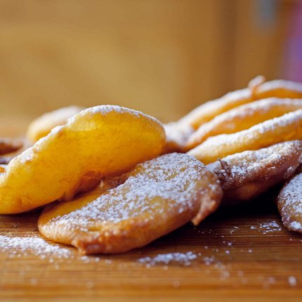 Fried sweet dough pieces dusted with powdered sugar on wooden board