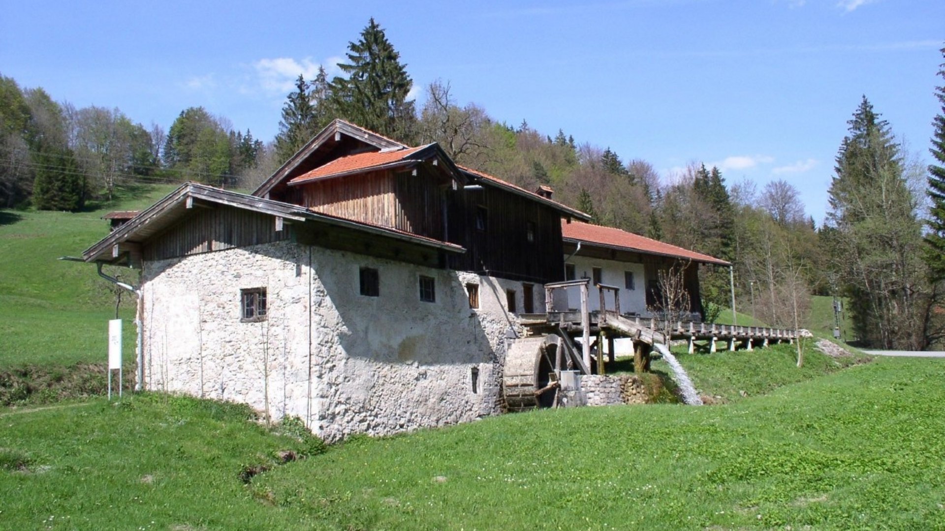 Old mill with water wheel in green landscape under clear sky