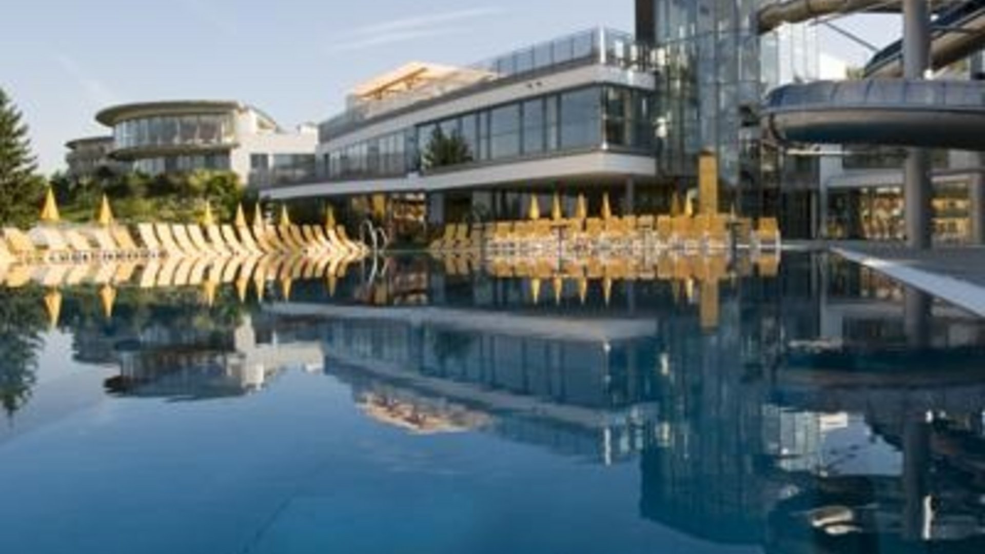Modern hotel with outdoor pool, lounge chairs and water slides under clear sky