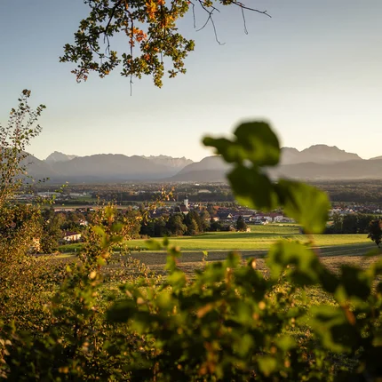 Uitzicht op groene velden, een dorp en bergen op de achtergrond bij zonsondergang