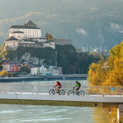 Top 5 Radtouren fürs Kufsteinerland © Mathäus Gartner Zwei Radfahrer auf einer Brücke mit Burg und herbstlichen Bäumen im Hintergrund