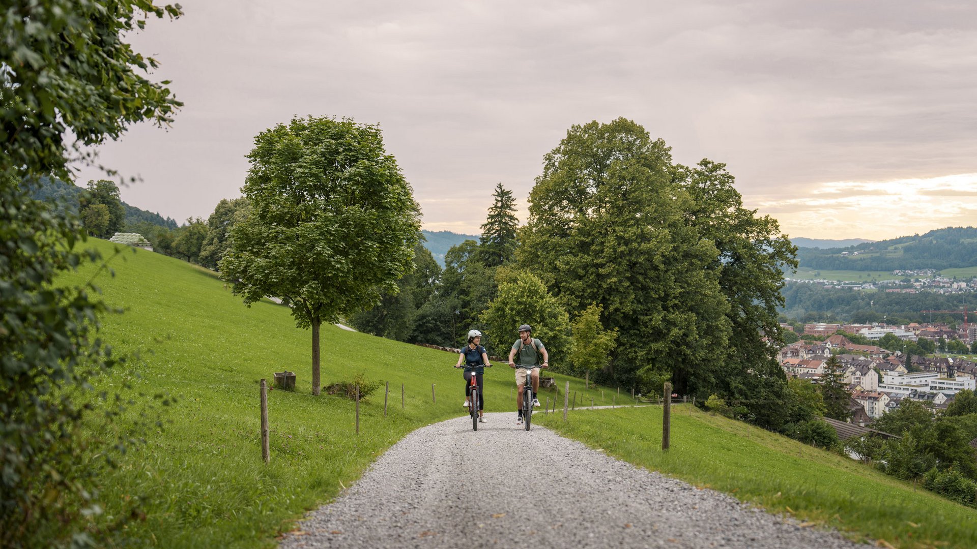 Two people cycling on a gravel path through green countryside