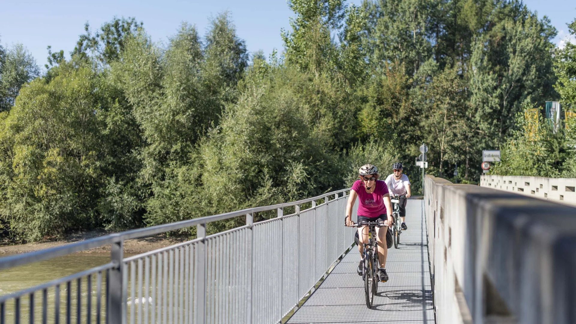 Twee mensen fietsen over een brug op een zonnige dag