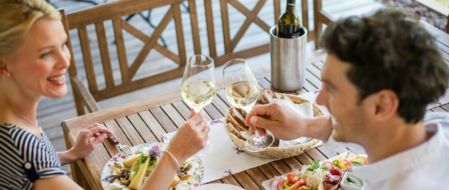 Paar stößt mit Weißweingläsern beim Essen im Freien an