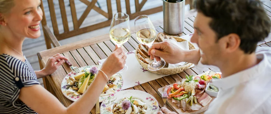 Paar stößt mit Weißweingläsern beim Essen im Freien an