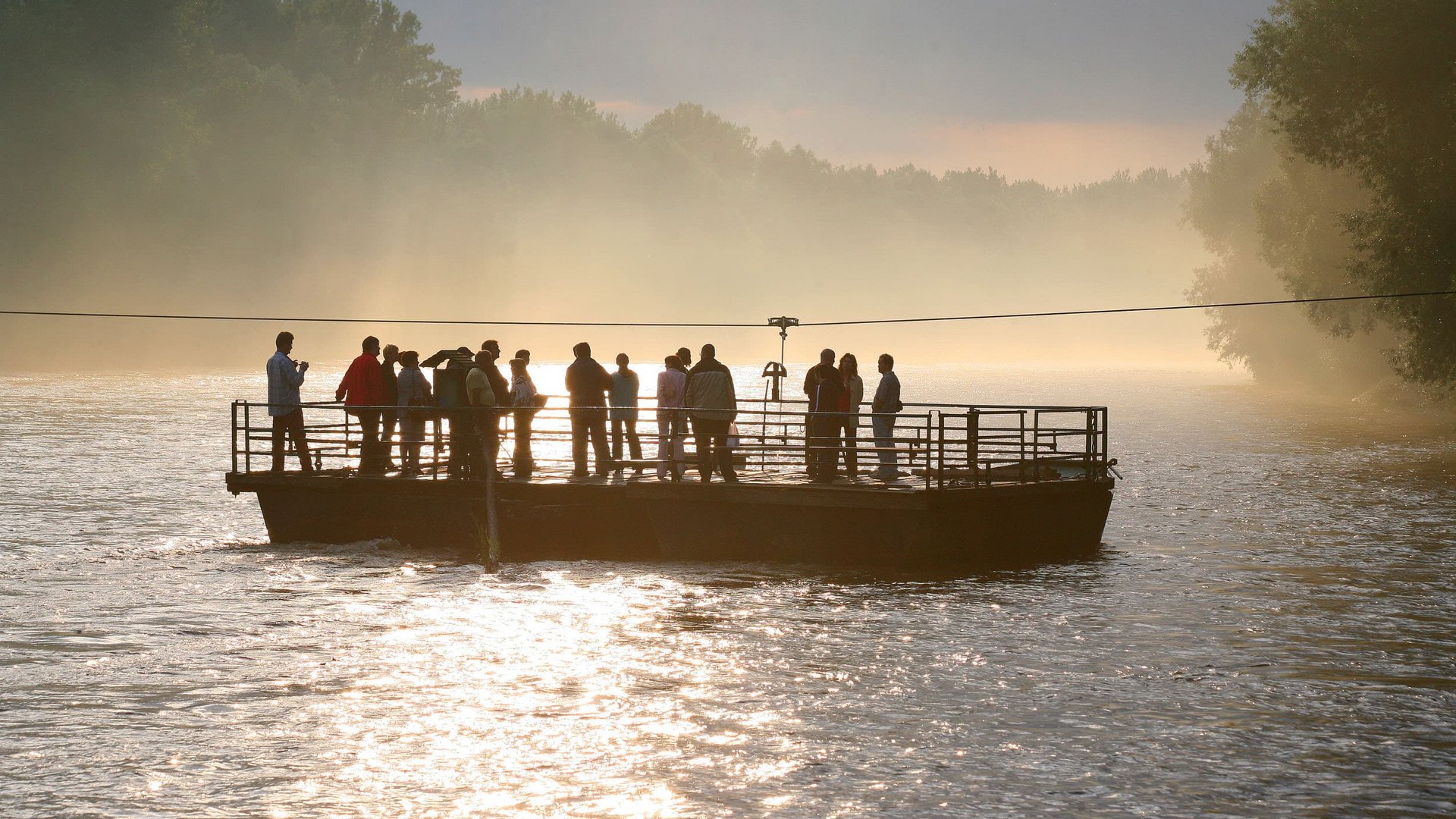 People on a ferry crossing a river at sunset