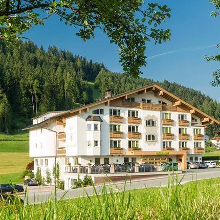 Hotel Thierseerhof Hotel building in green landscape with trees and mountains in the background
