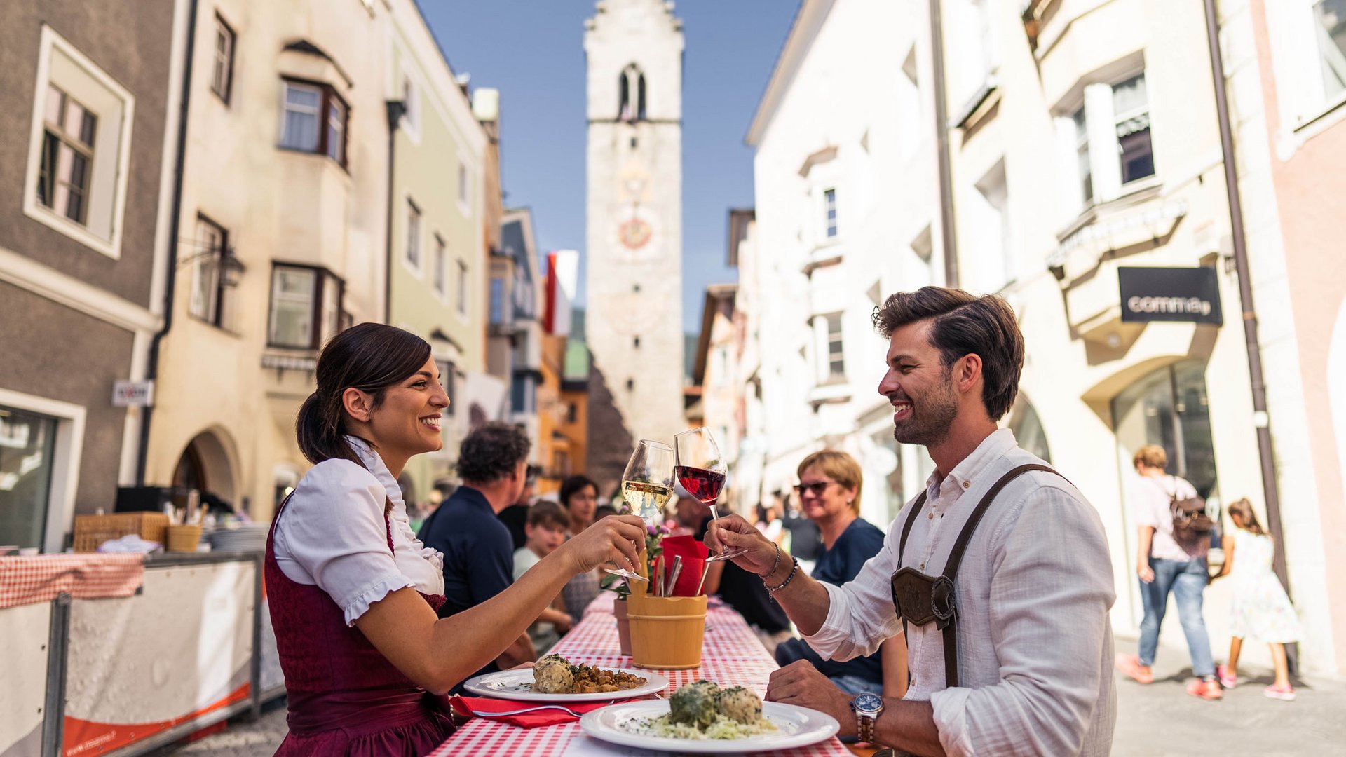 Couple clinking wine glasses while dining at an outdoor table in old town