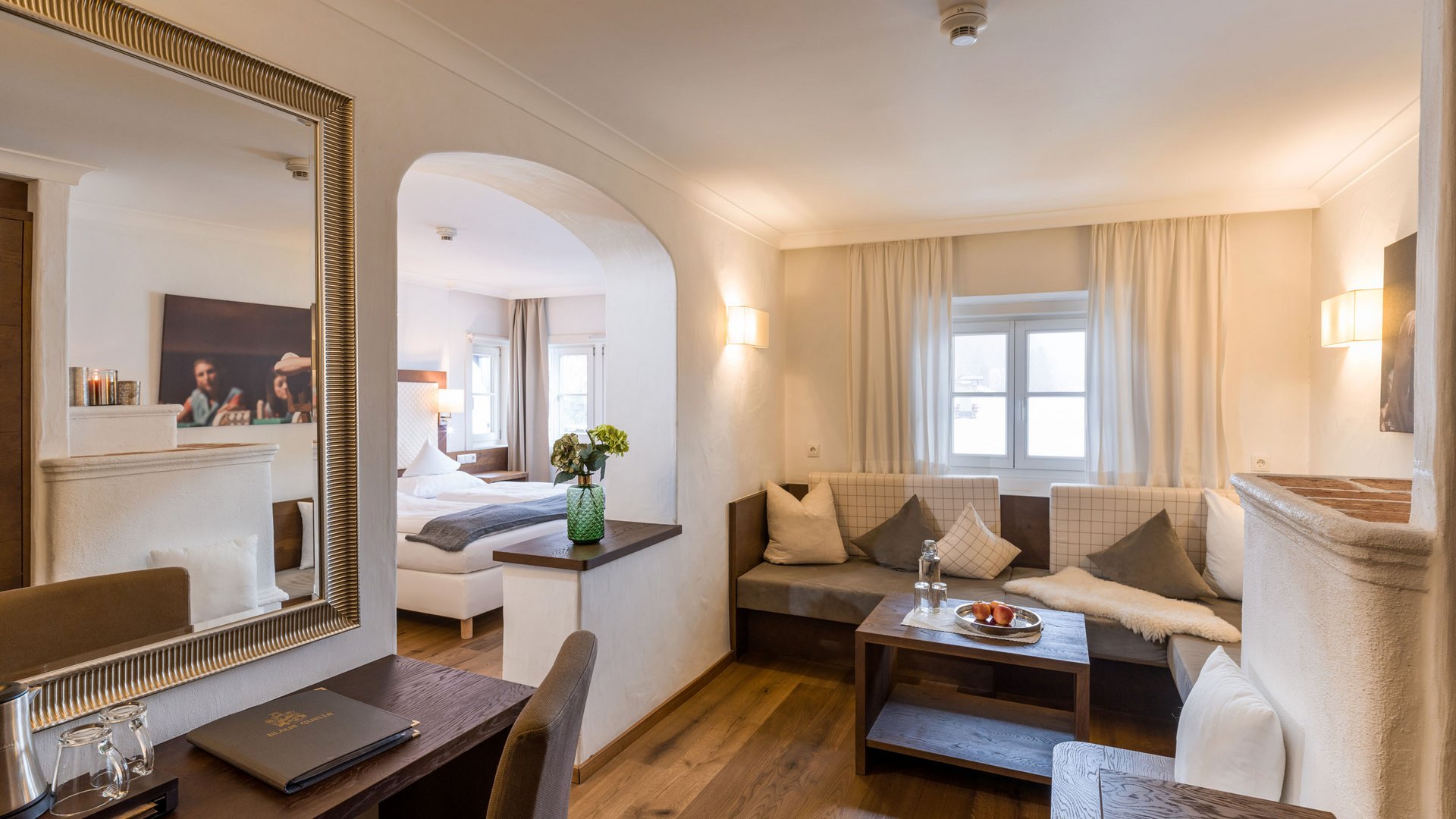 Cozy hotel room with seating area, desk, and a view into the bedroom