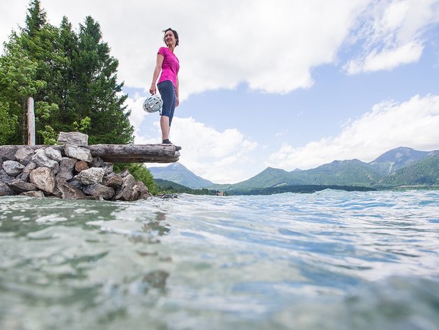 Frau in Sportkleidung hält Helm und blickt auf See und Berge