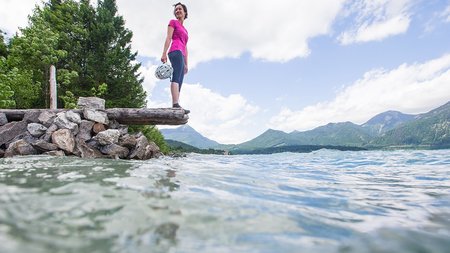 Frau in Sportkleidung hält Helm und blickt auf See und Berge