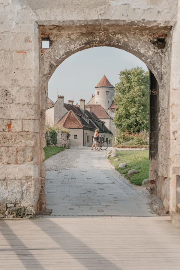 Blick durch einen alten Steinbogen auf einen Weg, Häuser und einen Turm