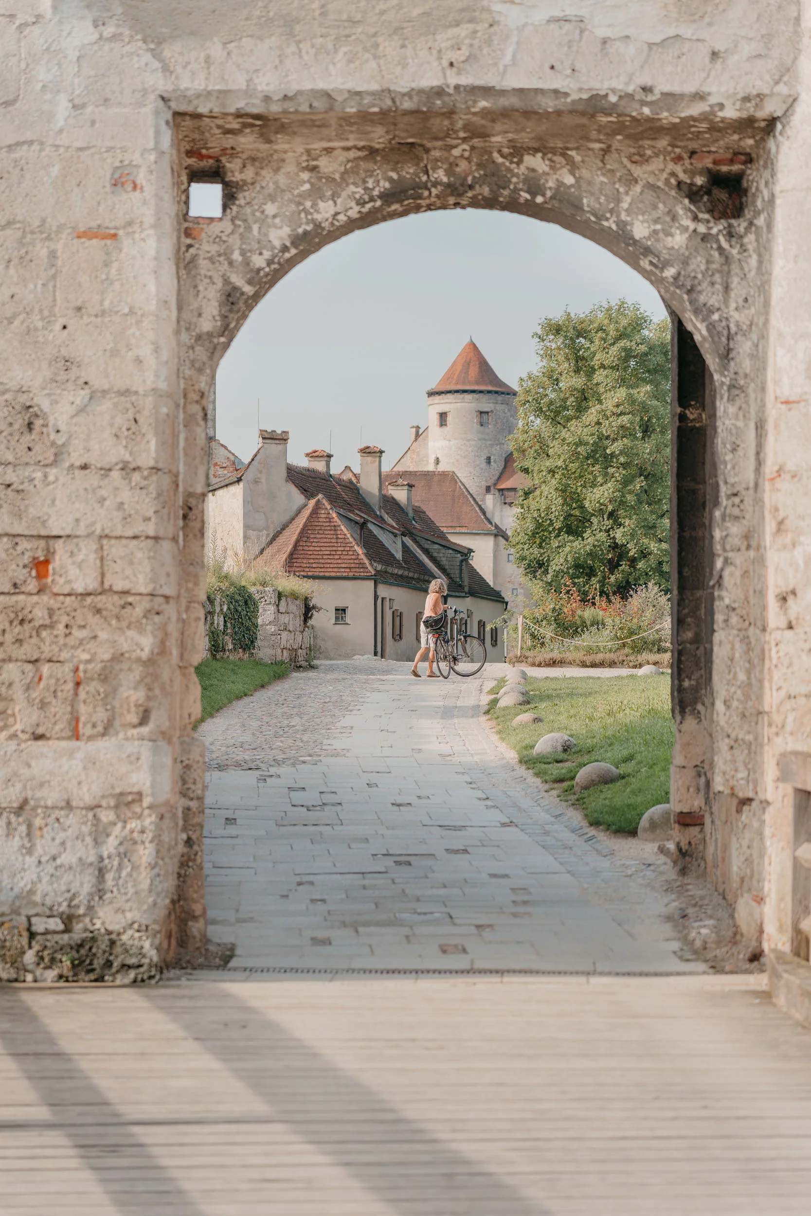 Blick durch einen alten Steinbogen auf einen Weg, Häuser und einen Turm