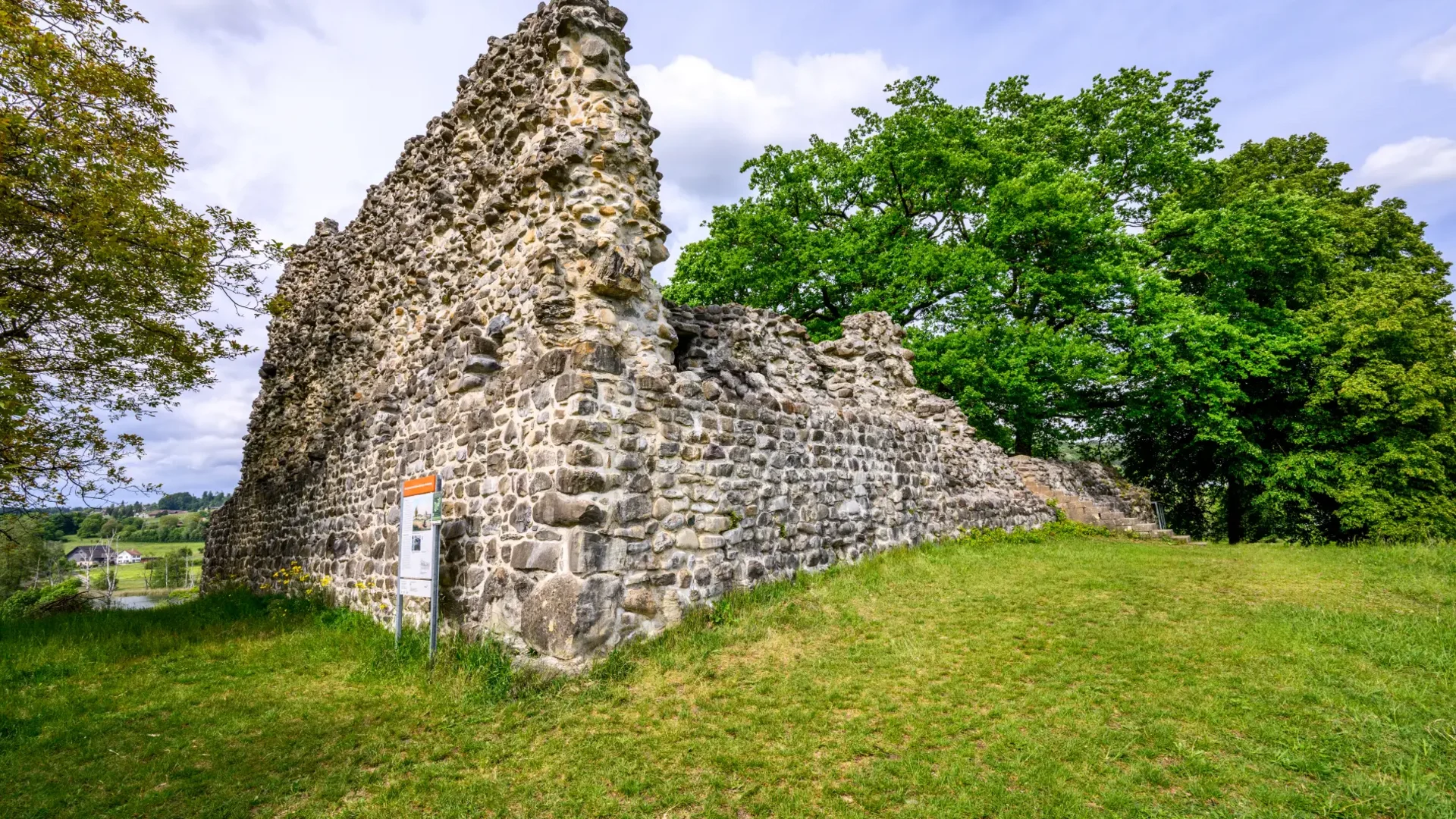 Tour-Detail © Balz Kubli Ruine einer alten Steinmauer umgeben von Gras und Bäumen unter blauem Himmel