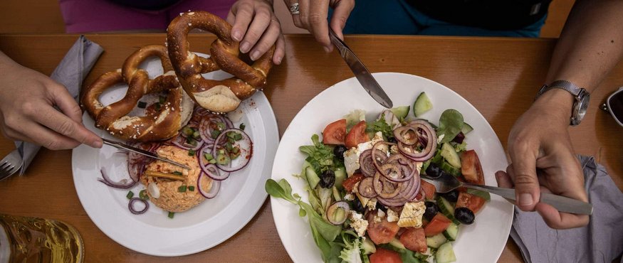 Two people eating pretzels and salad at a wooden table
