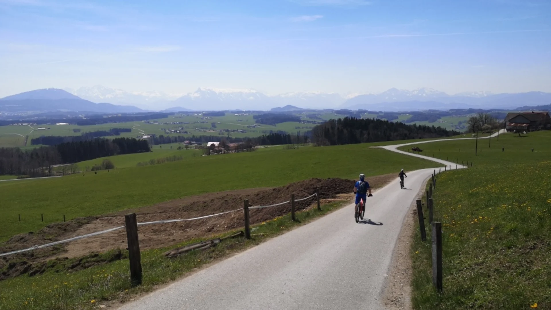 Ebike: Von den Salzachauen ins Salzburger Seenland © Bettina Bauer Zwei Radfahrer auf einer ländlichen Straße mit Bergen im Hintergrund