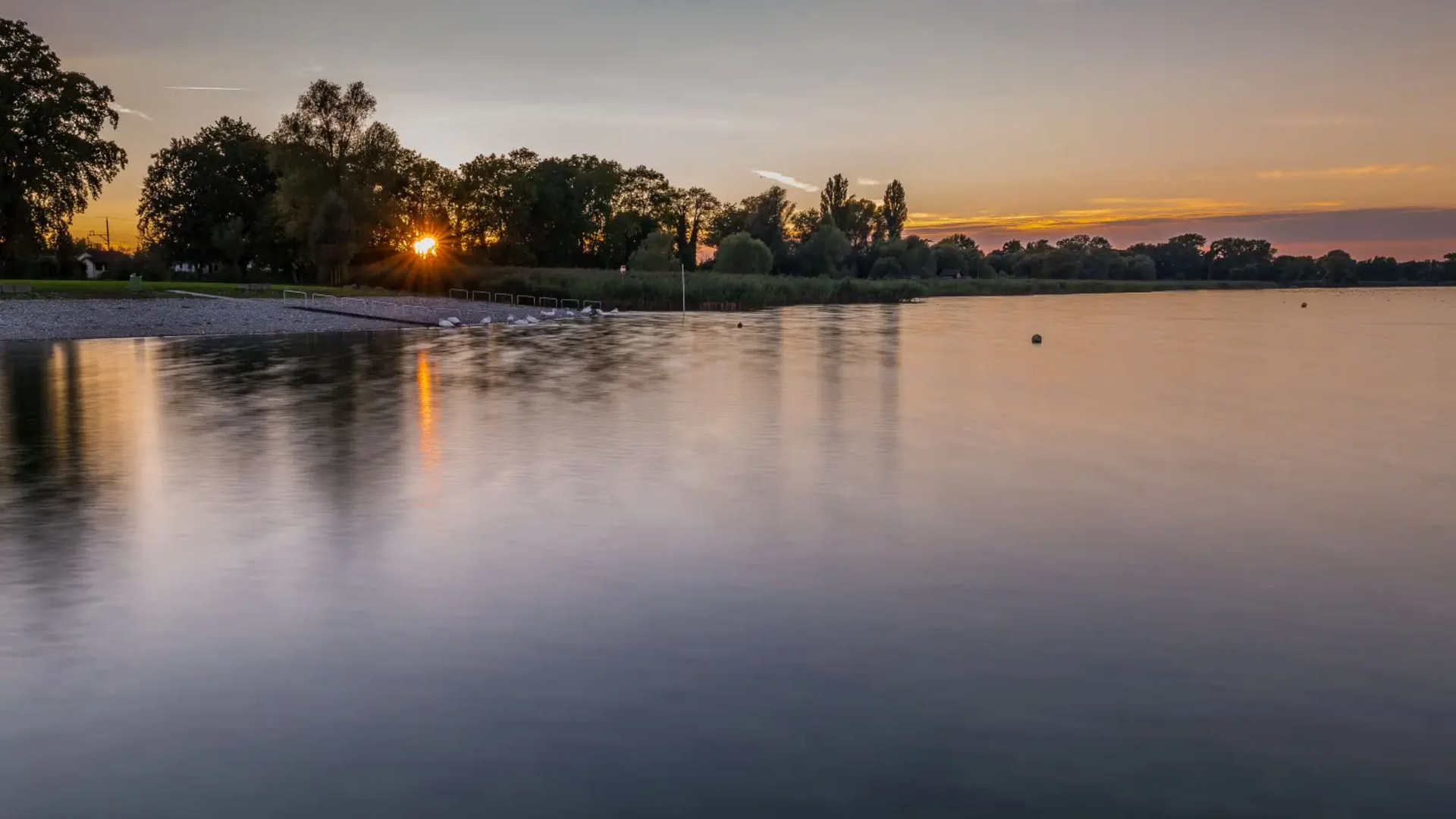 Sunset over a calm lake with trees along the shore