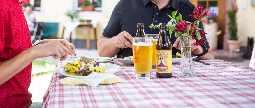 Herbstgenuss im Salzburger Seenland © Velontour Paar isst draußen im Biergarten mit Essen und Bier vor einem Gasthof