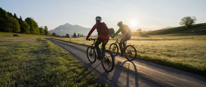 Two cyclists riding on country road at sunrise