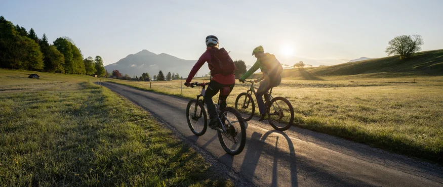 Zwei Radfahrer fahren auf Landstraße bei Sonnenaufgang