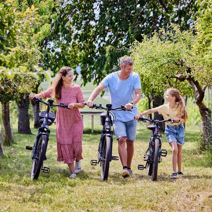 Familie mit Fahrrädern spaziert durch einen Baumgarten